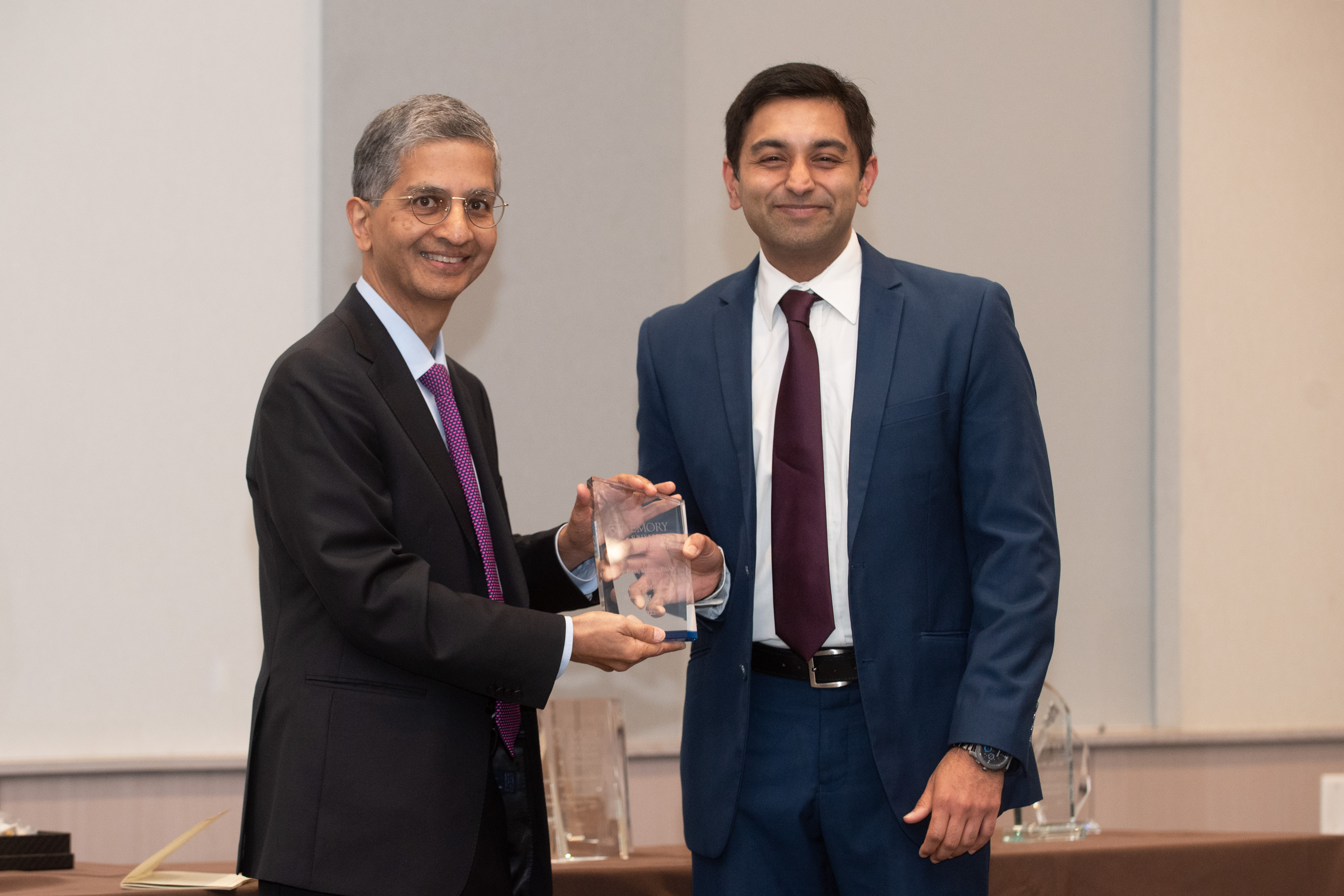 Two people standing; one holding a glass award