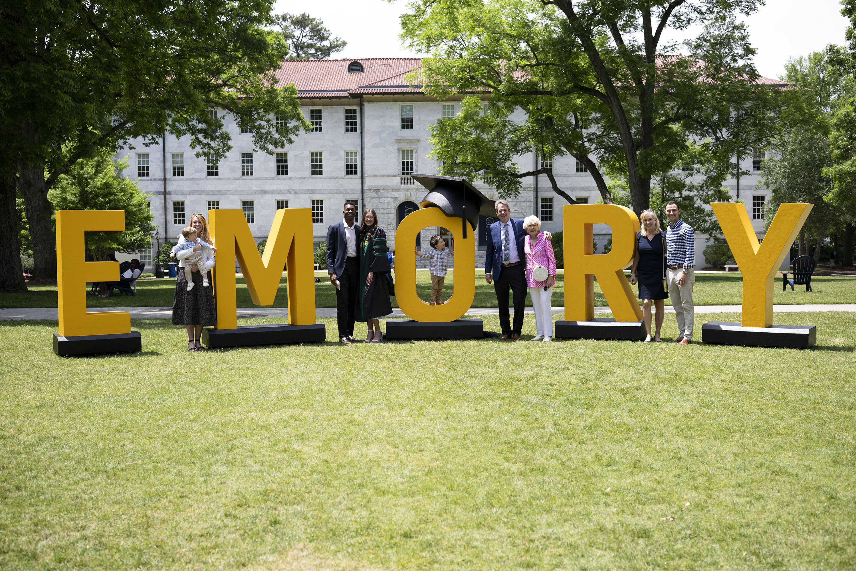 Graduates in regalia standing in front of huge EMORY letters on the grassy quad
