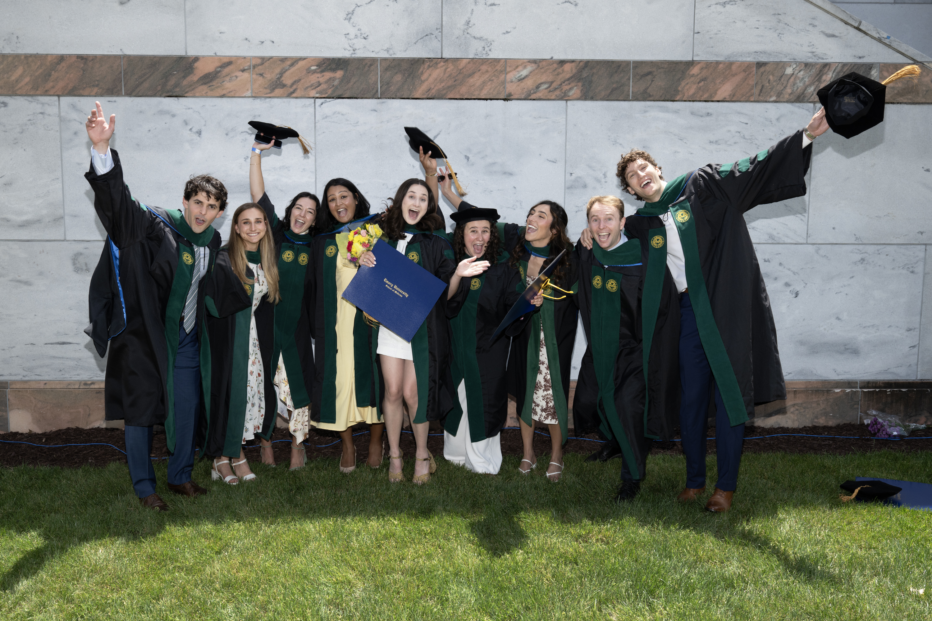 large group of graduates smiling and folder large blue folders
