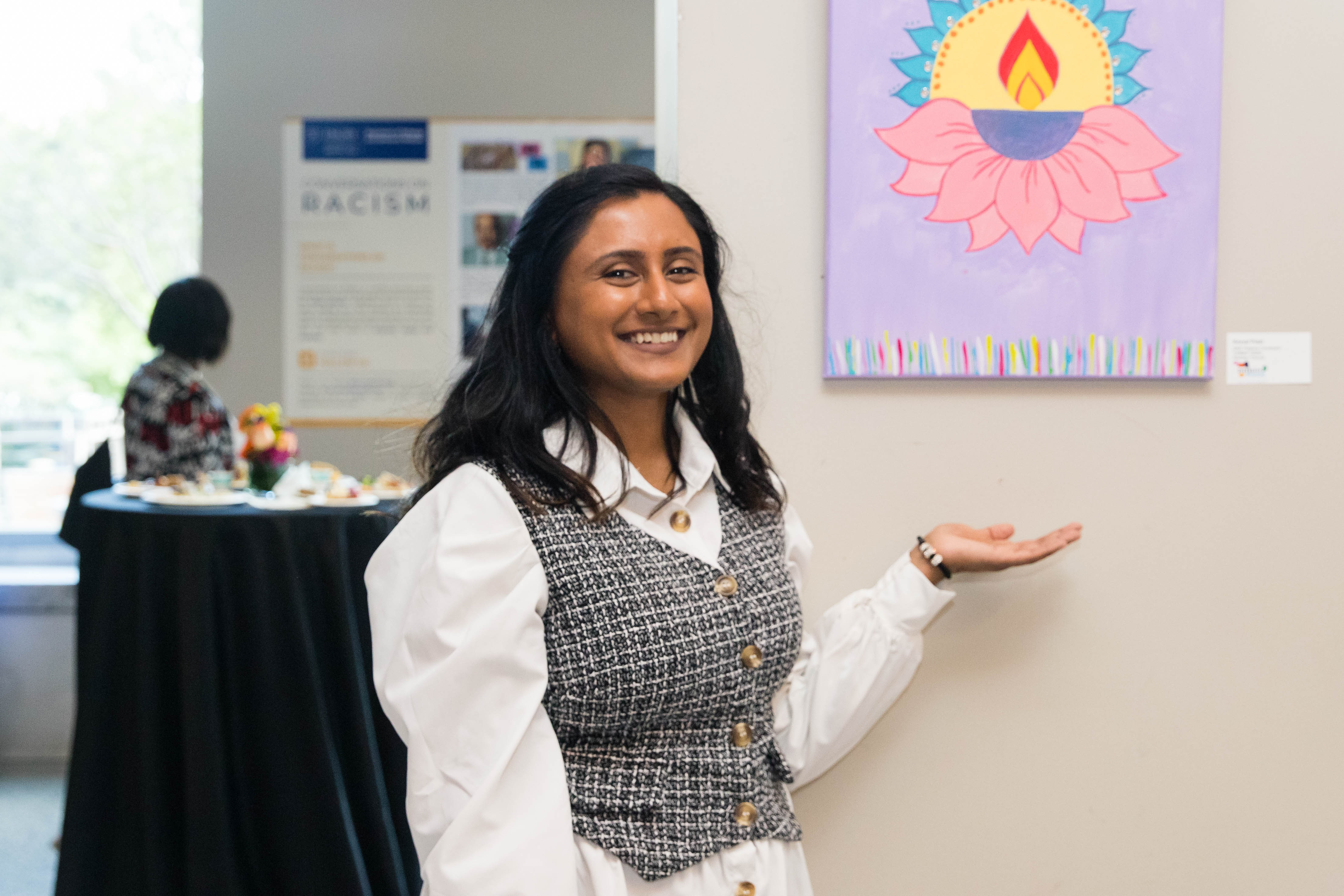 A woman stands in front of her art work hung on the wall