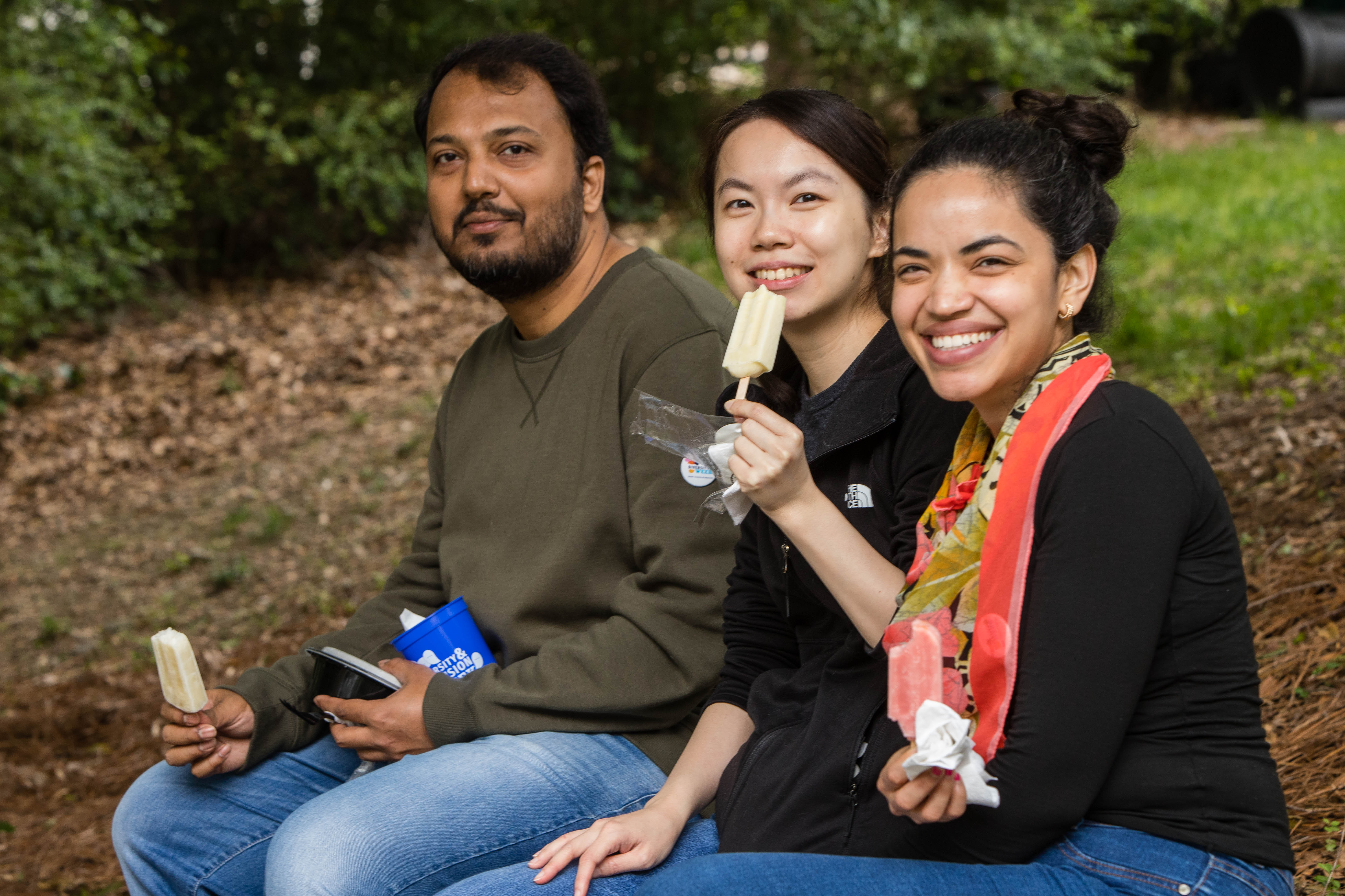 Three people sit down and eat popsicles