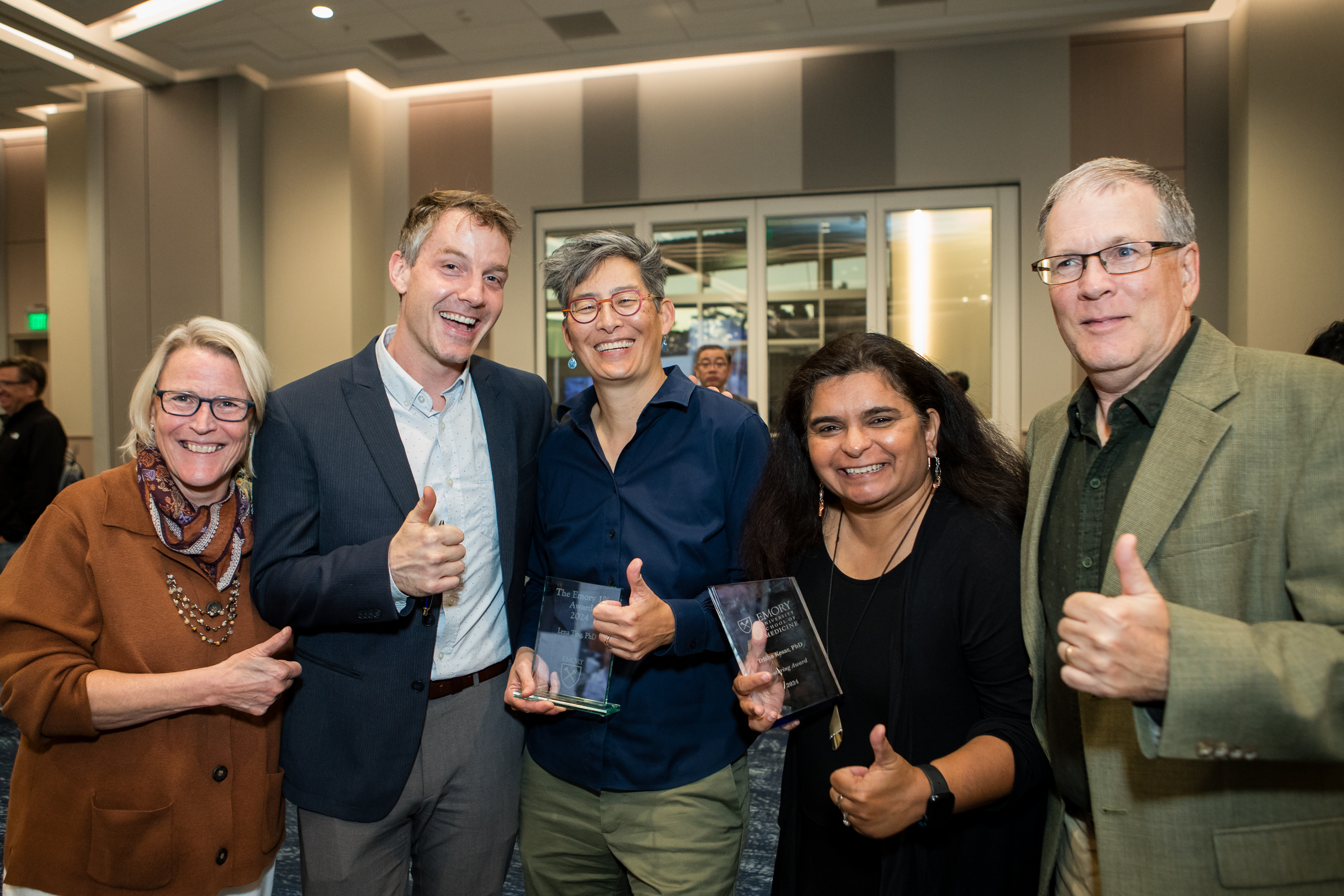 Five people smile for a photo some holding awards and others giving thumbs up.