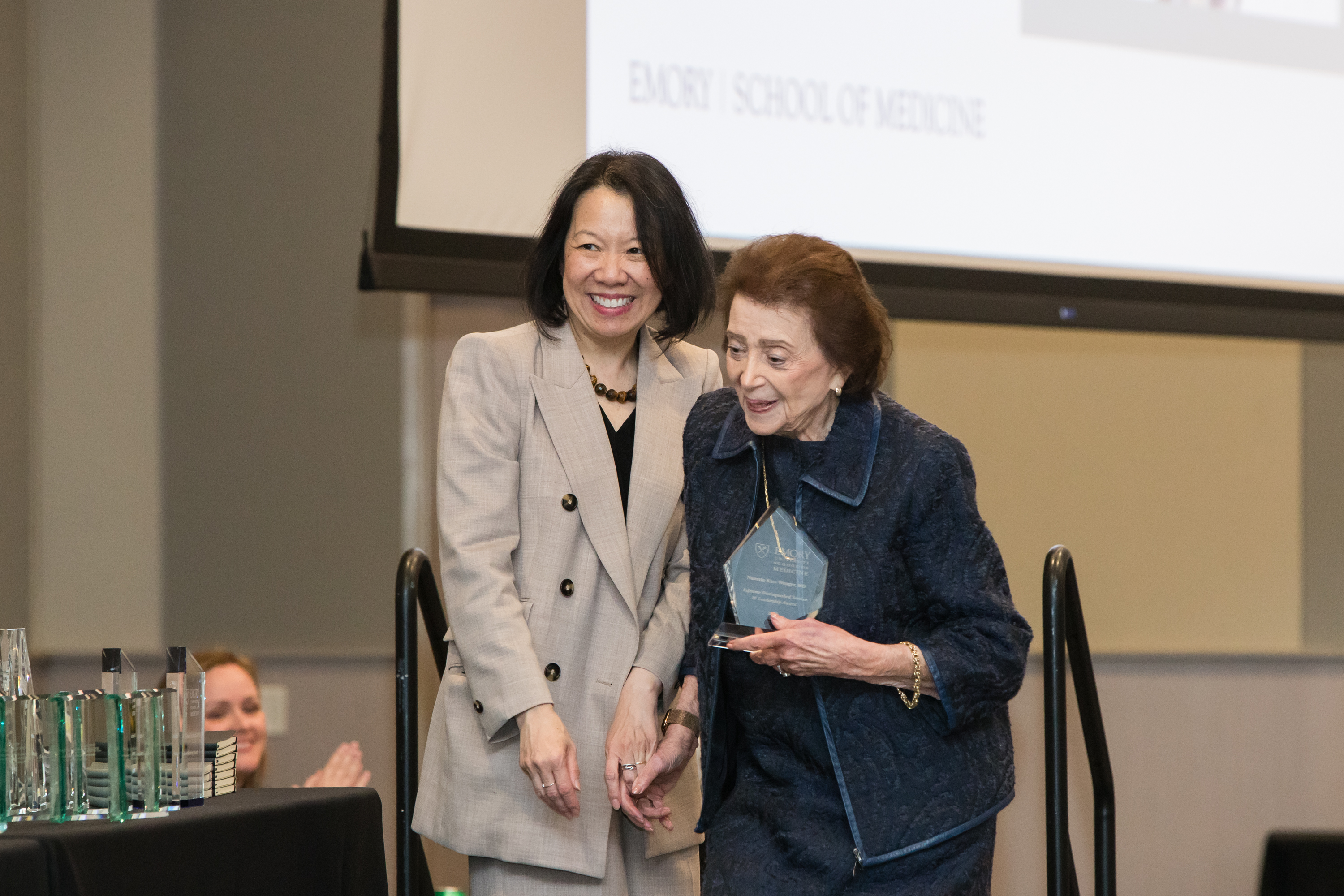 Dean Wong stands on stage with Nanette Wenger who accepts an award.