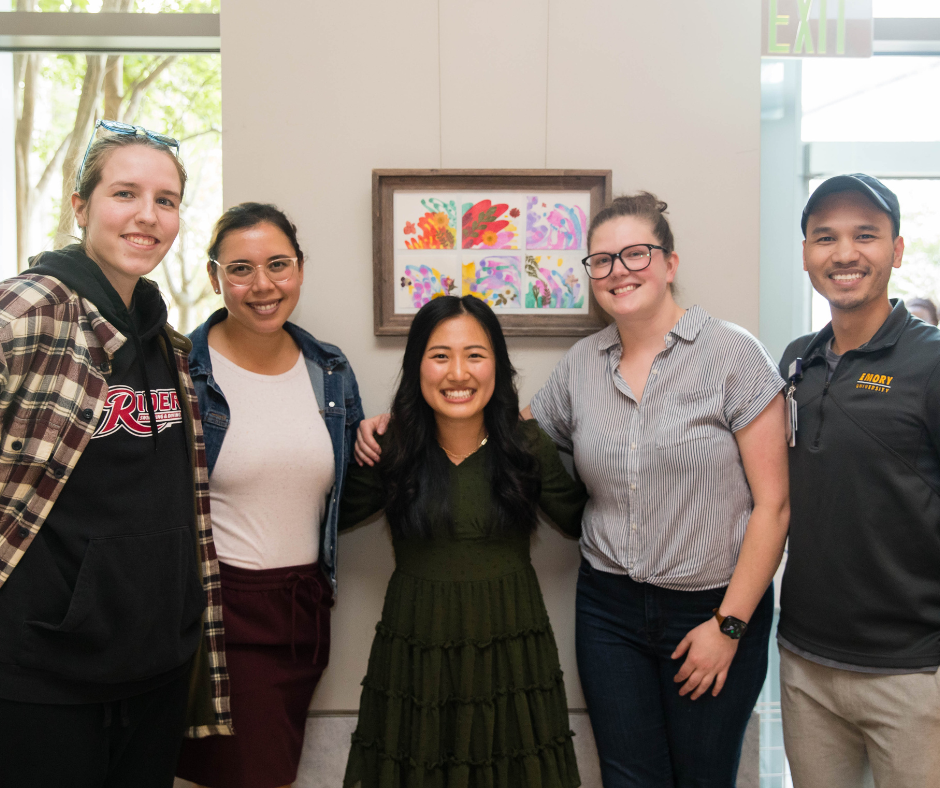 Four people stand in front of artwork hung on the wall. 