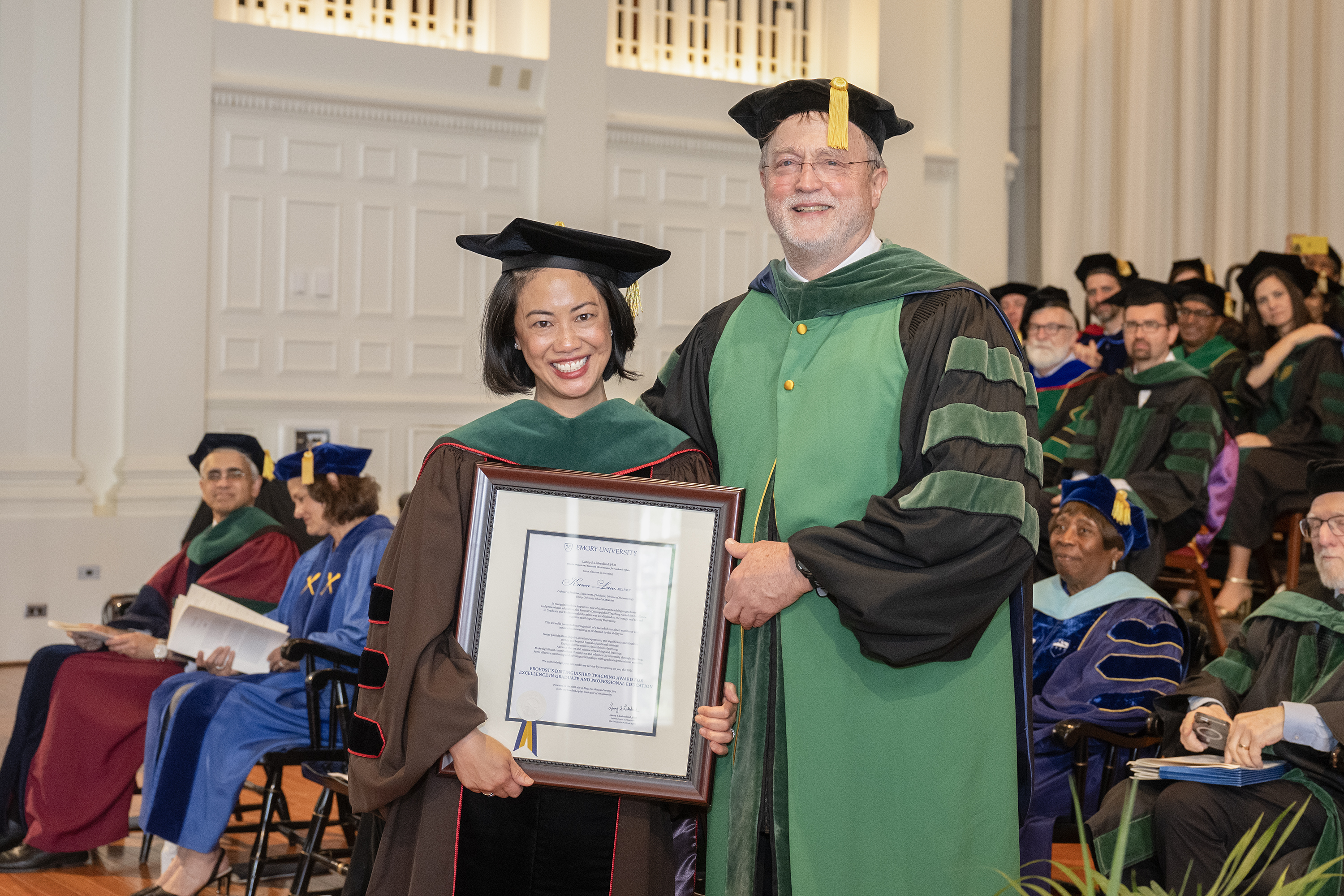 two people in graduation robes and one holding an award