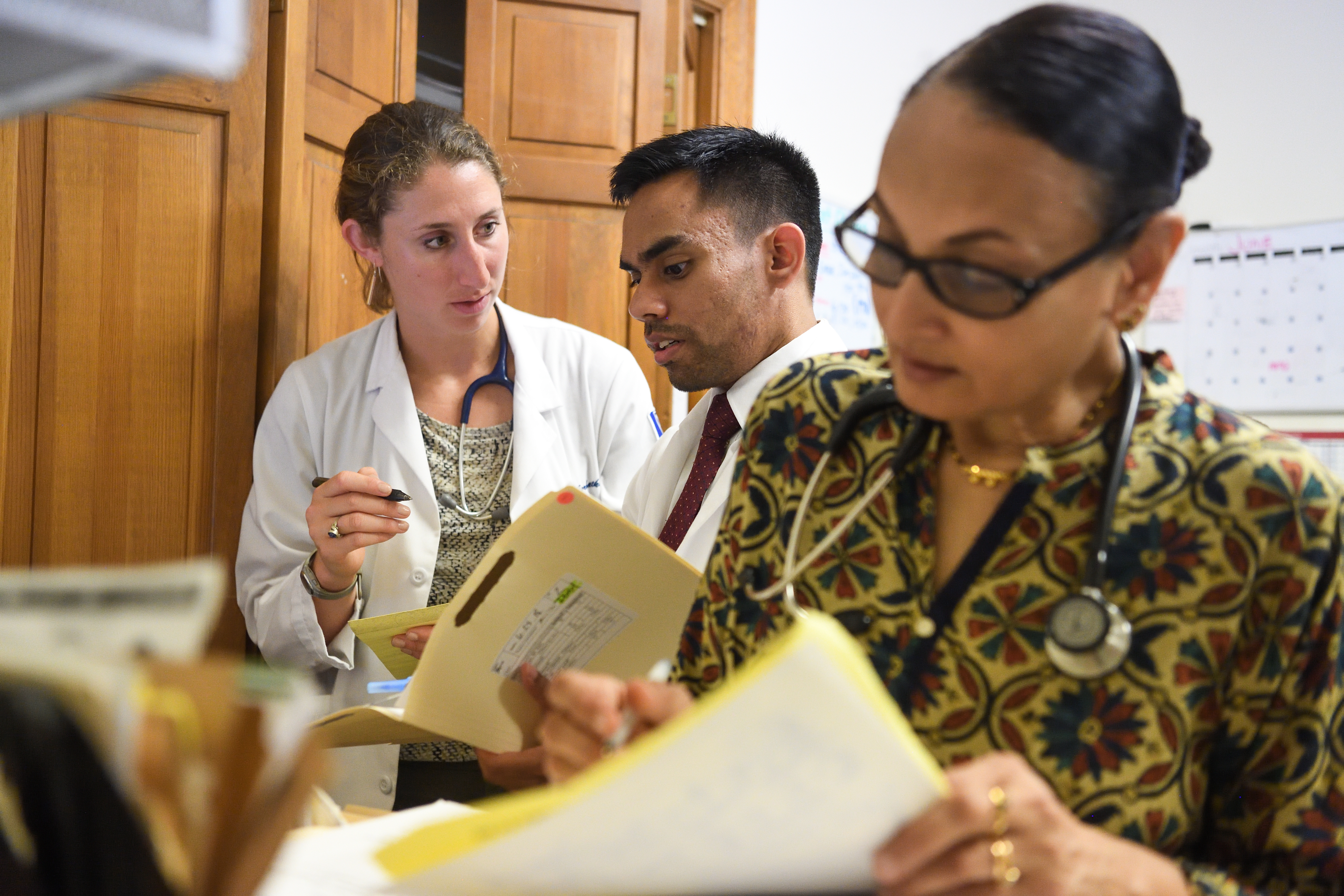 Two physicians review file while another writes notes