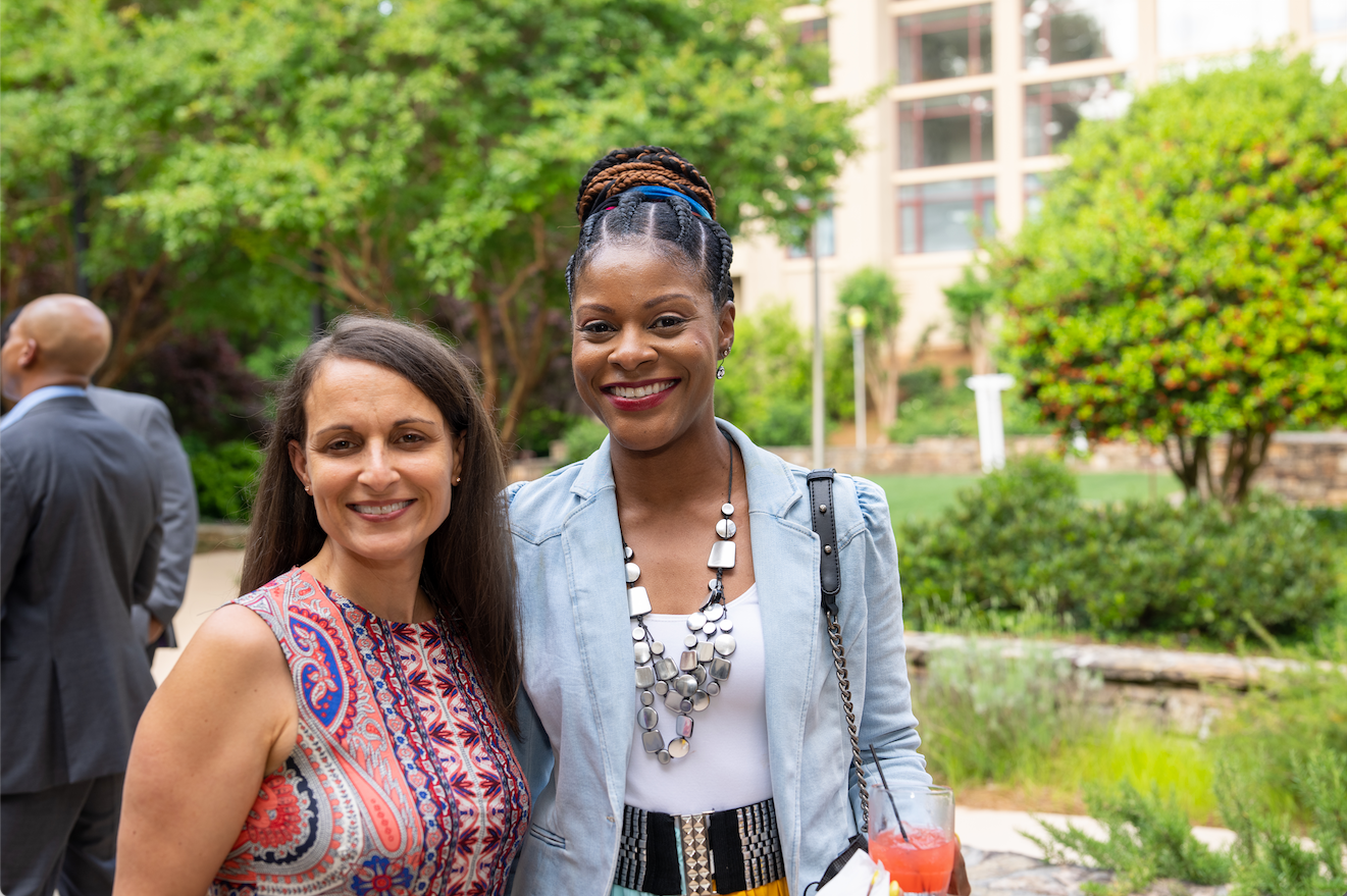 Two women faculty smile for photo at a gathering