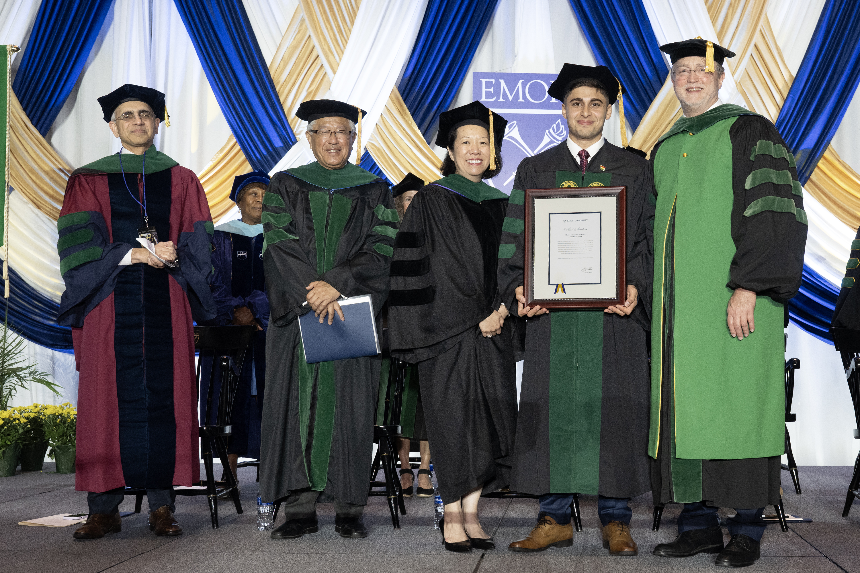 People on stage in caps and gowns presenting an award