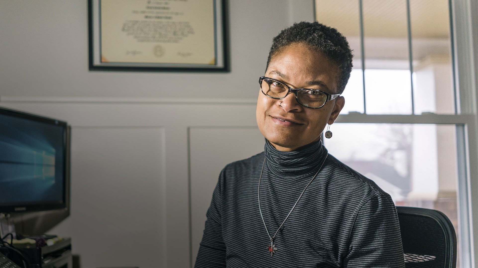 Tonia Poteat smiling in front of a framed degree and a computer