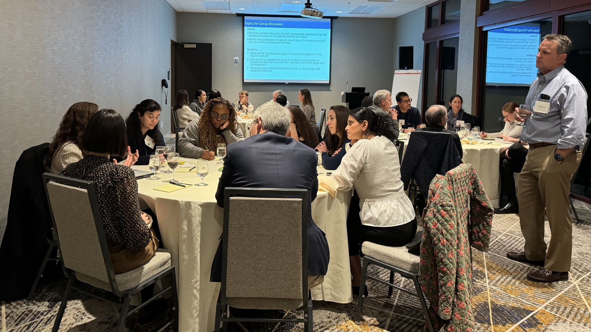 Dr. David Roberts standing and talking to a room of AIM Center faculty seated at round tables