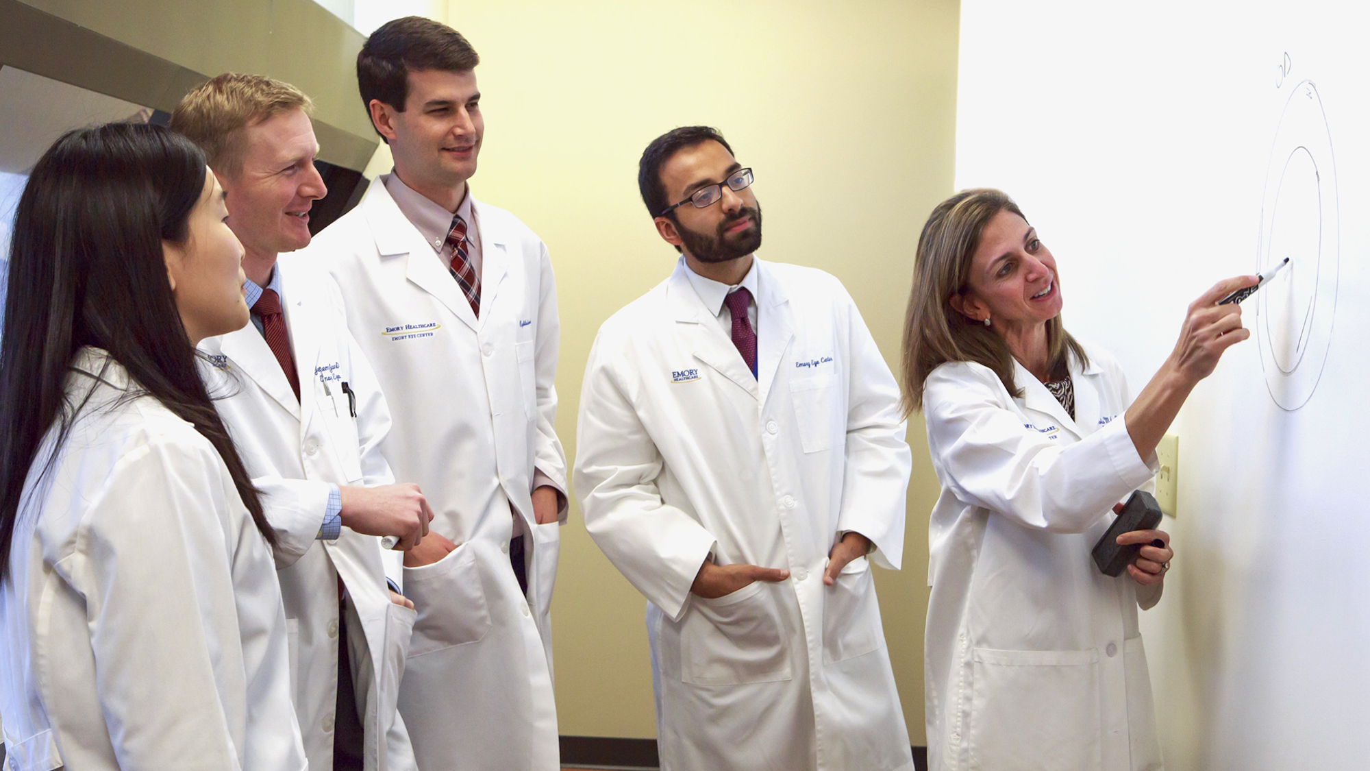 Five doctors discussing a presentation on a white board