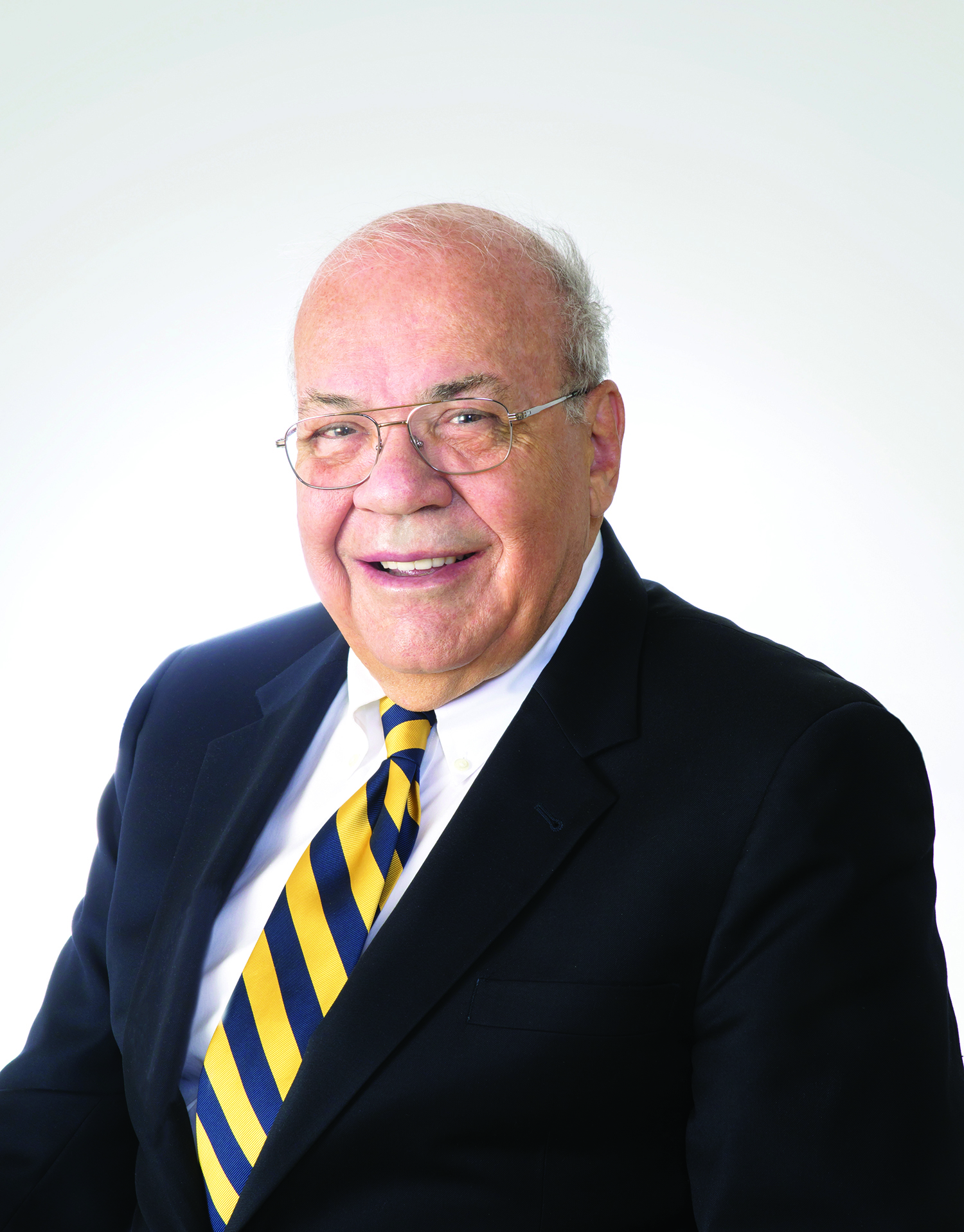 smiling person wearing a dark suit jacket over a white shirt and striped tie