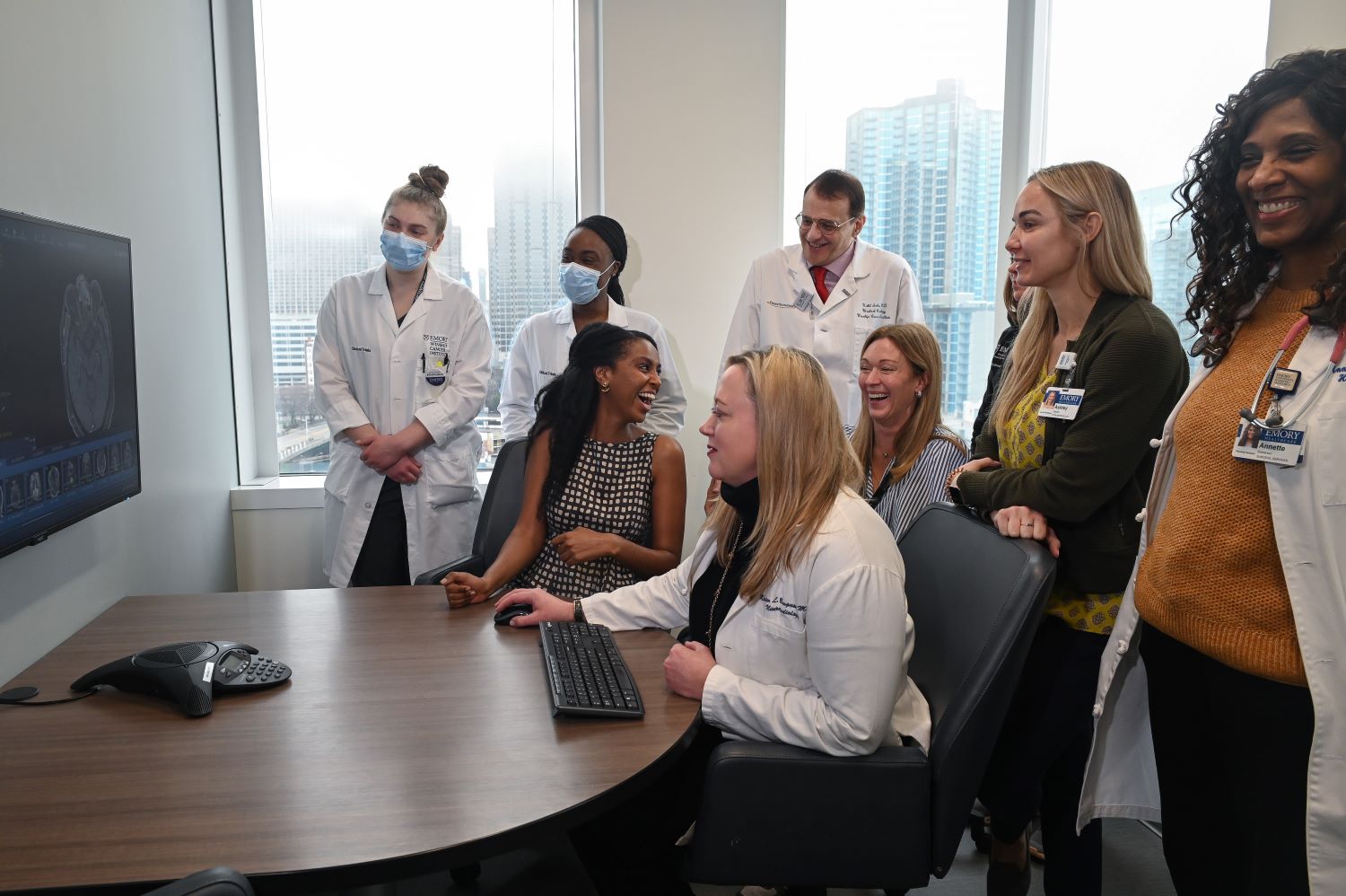 men and women wearing work clothes and some with white doctor coats smiling and talking with each other in a room that shows city buildings shrouded in light fog