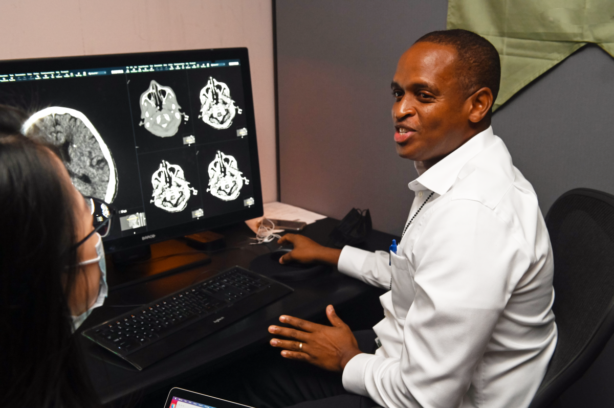 man with cropped black hair talking to woman while in front of computer images of brain