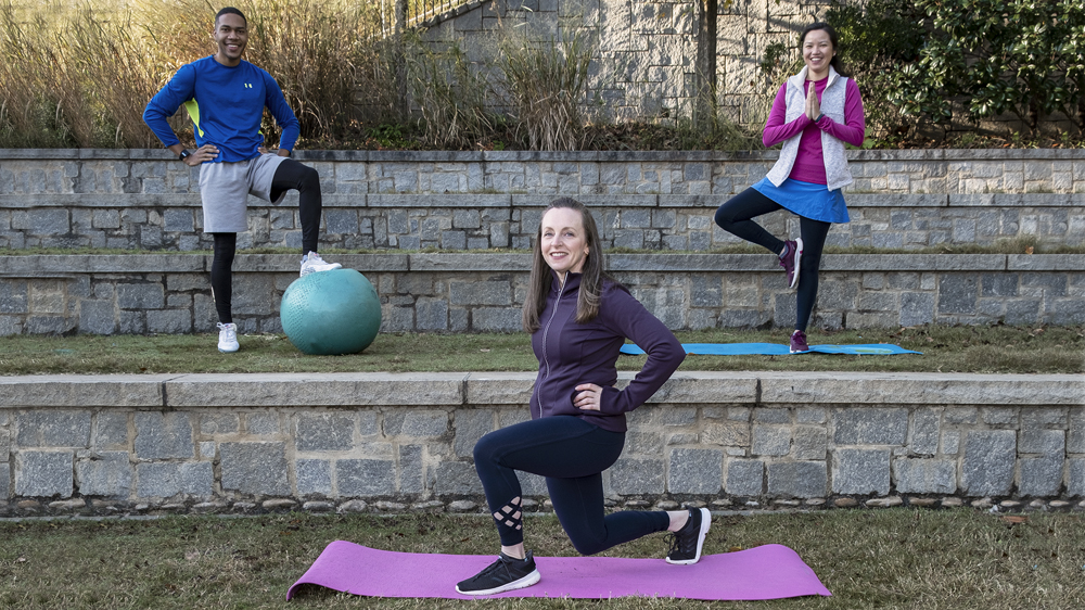 man with foot resting on exercise ball while a woman stands on one foot and balances other foot against the inner knee and another woman is on one knee and smiling