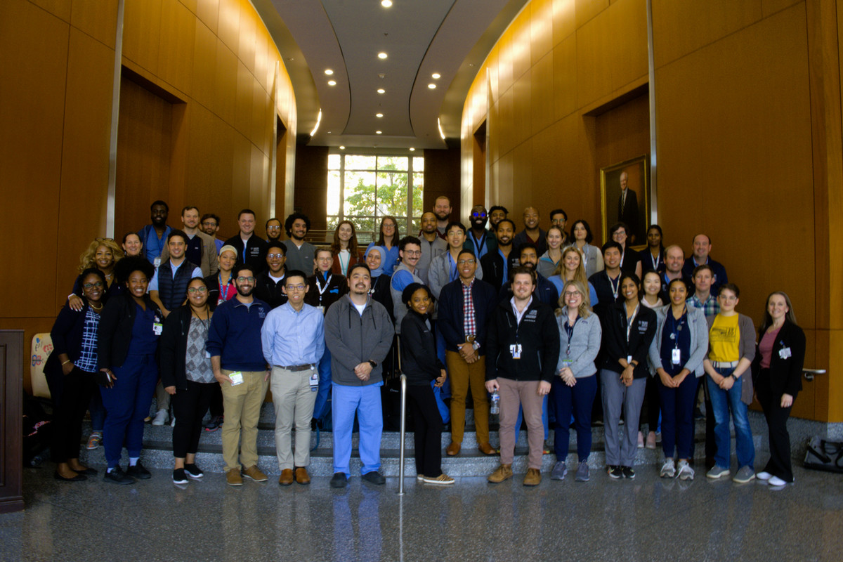 radiology residents and faculty standing smiling in a large hall paneled in wood
