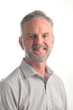 smiling man with short silver and dark hair and beard and moustache wearing a light grey shirt