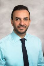 smiling man with short dark hair and light bear and moustache wearing an aqua dress shirt with narrow dark tie