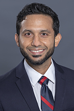 smiling man with short dark hair and beard wearing white shirt red and grey striped tie and dark suit jacket