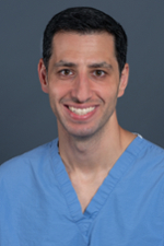 smiling person with short dark hair wearing a blue scrubs shirt