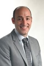 smiling man wearing a medium grey suit jacket over a white shirt and grey tie