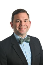 smiling person wearing a green bowtie with a black suit jacket and blue shirt