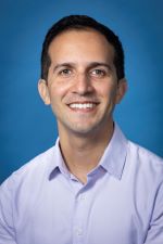 smiling man with short dark hair wearing a light lavendar open collar shirt