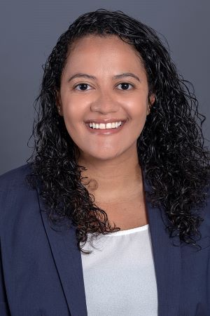 smiling person with long dark wavy hair wearing a blue jacket over a white blouse