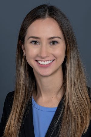 smiling person with long blond hair over both shoulders wearign a dark blue jacket over a cerulean blouse