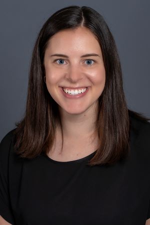 smiling person with shoulder length brown hair wearing a black top