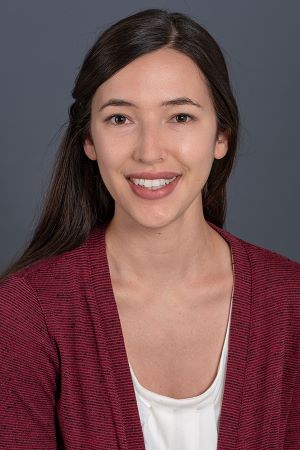 smiling person with long brown hair wearing a red cardigan over a white blouse