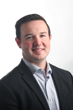 smiling man with short brown hair and wearing a dark suit jacket over a white shirt