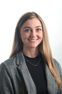 smiling woman with long blond hair and wearing a grey and black plaid jacket over a black top