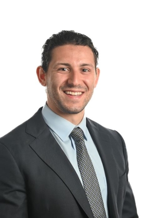 smiling person wearing grey suit jacket and tie over a lighter grey shirt