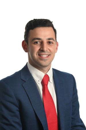 smiling person wearing dark blue suit jacket over a white shirt and red tie