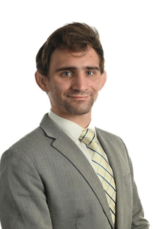 smiling person wearing green suit jacket over a light shirt and yellow and green striped tie