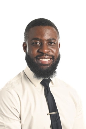 smiling person with black beard wearing a cream dress shirt and dark brown tie