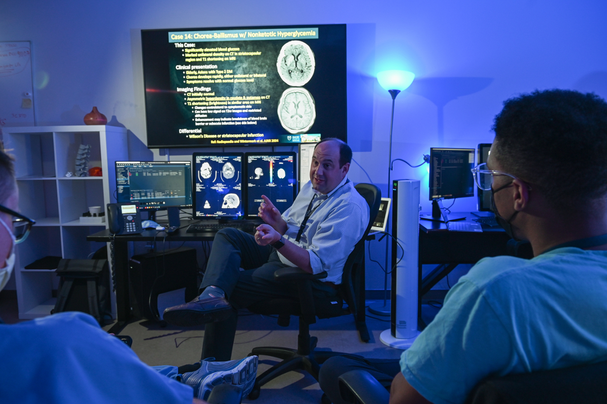 person talking to class in a blue room with images of a brain behind them