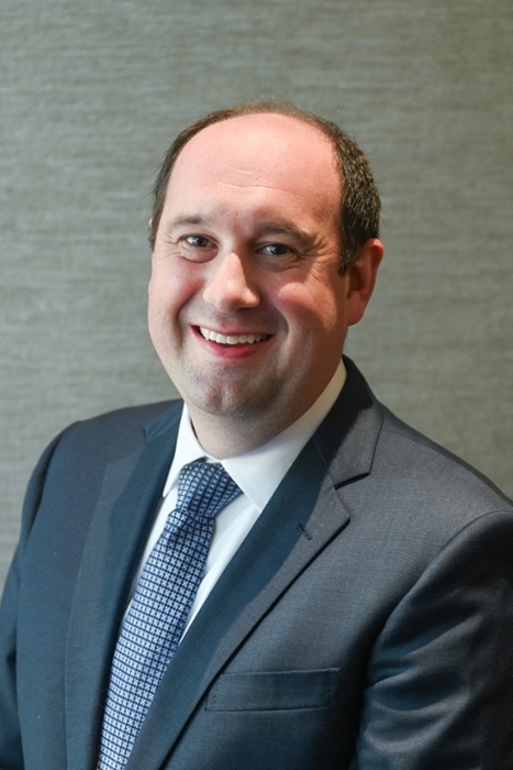 smiling person wearing a blue suit coat over a white shirt and blue patternedtie