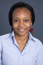 smiling woman whose black hair is pulled back and has pink braided ends is wearing a blue denim shirt and smiling