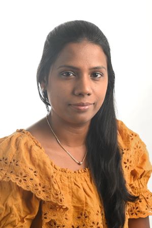 faintly smiling woman with long dark hair cascading over one shoulder wearing an orange ruffled top and gold necklace