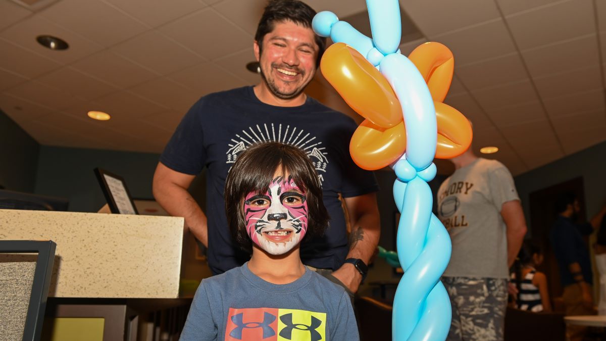 smiling child with face painted like a cat and holding balloons