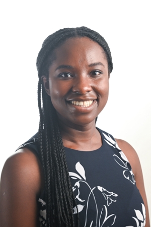 smiling woman with long black braids falling over one shoulder wearing a black and white floral print top