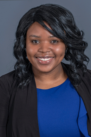 smiling woman with black hair falling in soft curls around her face to her shoulders wearing a royal blue top under a black suit jacket