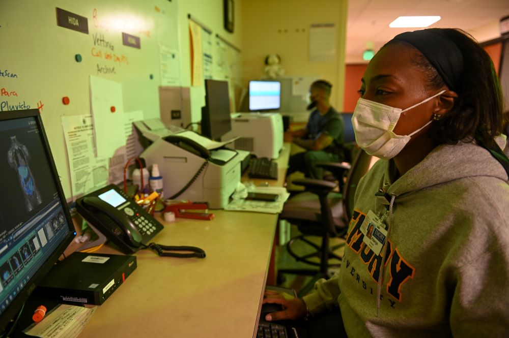 woman wearing mask and Emory sweatshirt looking at nuclear medicine images on computer