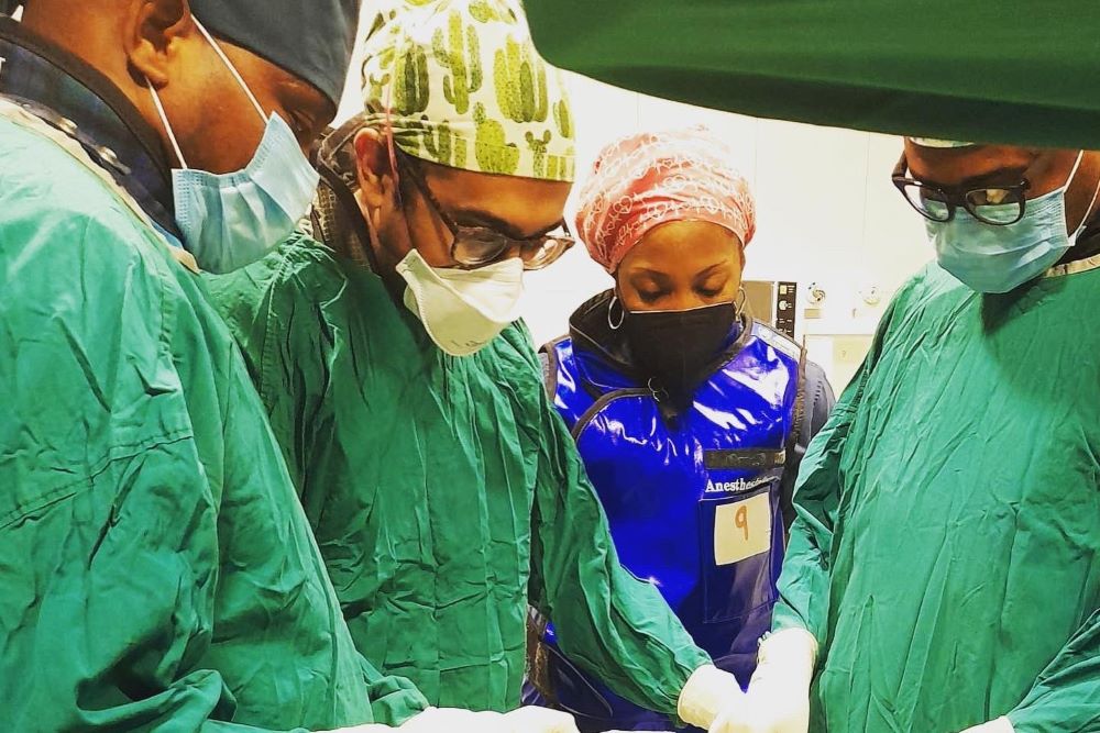 men and women wearing green gowns and masks performing a procedure