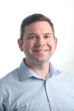smiling man with light brown hair wearing a light blue checked shirt