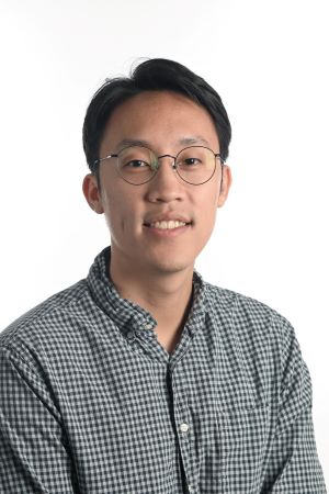 smiling person with round spectacles wearing a grey checked shirt