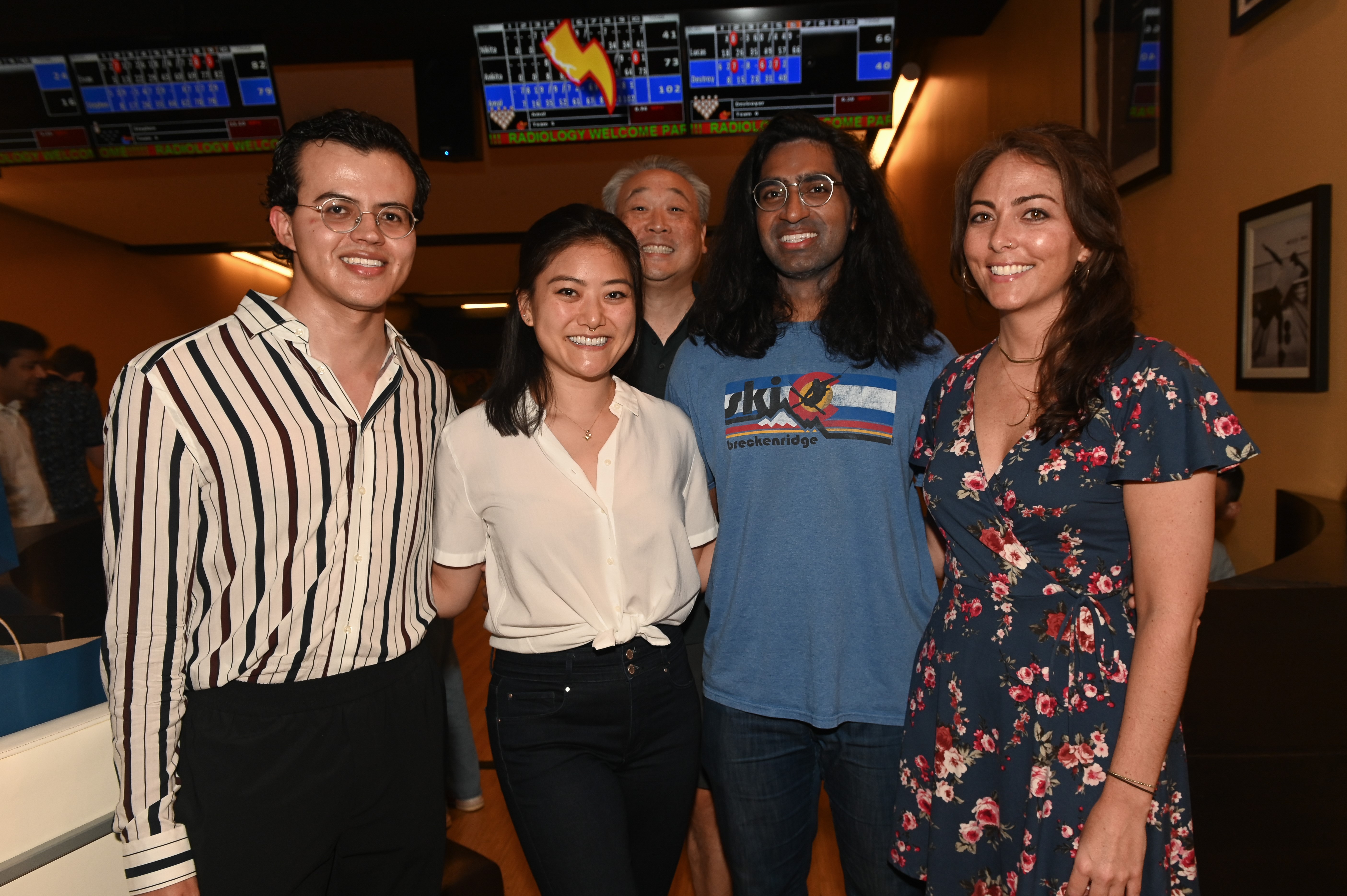 smiling people in a line with their arms around each other and one standing in back smiling