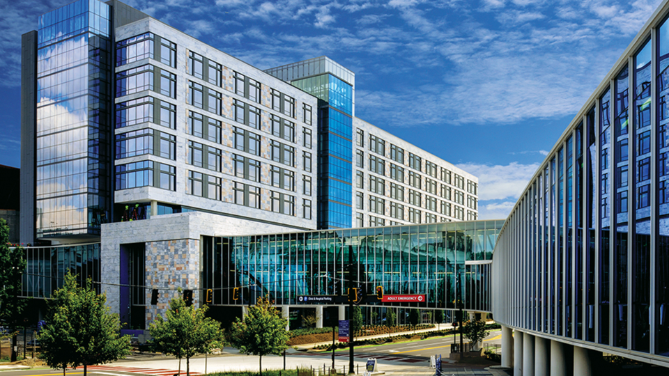 tall building made of glass and granite with glass walkway stretching across 4-lane street with blue skies overhead